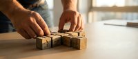 Male carpenter hands arranging wooden alphabet blocks on workshop table. Craftsmanship and woodworking tools for educational toys and learning materials.