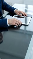 Businessman hands using digital tablet on glass desk in modern office for professional work and technology communication.