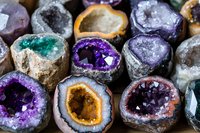 Collection of colorful natural crystal geodes and mineral specimens displaying vibrant purple amethyst, green and orange formations for geology education.