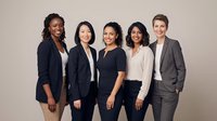 Diverse group of five professional women in business casual attire standing together against neutral background, representing corporate teamwork and workplace diversity for business and corporate projects.