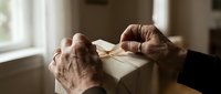 Senior male hands opening cream-colored envelope indoors with natural window light, conveying anticipation and correspondence moment for mail, communication, and administrative themes.