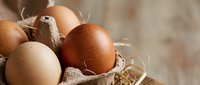 Fresh brown and beige chicken eggs in rustic cardboard carton with natural straw on wooden surface for organic farm cooking and baking ingredients.
