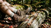 Hiker resting worn leather boots on fallen log during autumn forest trek. Outdoor adventure and nature exploration concept for camping and hiking enthusiasts.