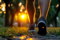 Running shoes on wet path at sunset with bokeh lights and puddle reflections creating atmospheric outdoor scene. Active lifestyle in nature setting.