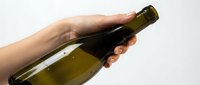 Hand holding dark glass bottle with olive oil or wine against white background, suitable for beverage packaging, culinary content, and product marketing materials.
