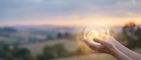 Hand holding glowing light bulb against sunset landscape representing innovation, creativity and bright ideas for business solutions.