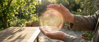 Hands protecting glowing energy sphere in sunlit garden setting symbolizing environmental conservation, renewable energy, and sustainable future concepts.