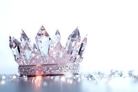 Crystal crown with delicate gems and diamonds on reflective surface in soft pink and blue lighting, creating magical royal atmosphere with bokeh effect.