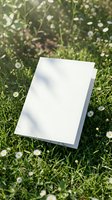 Blank white paper card mockup on green grass with small white daisies and natural sunlight shadows for branding and design projects.