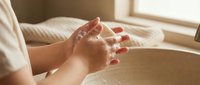 Pregnant woman gently holding her belly in soft morning light, expecting mother touching bump in cozy bedroom setting for maternity and pregnancy concepts.