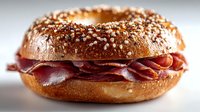 Freshly baked everything bagel with crispy bacon strips on sesame seed topped bread roll. Breakfast sandwich ready for morning meal or brunch menu.