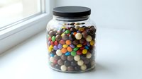 Glass jar filled with colorful chocolate candies on white windowsill for kitchen storage and sweet treats display.