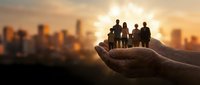 Protective hands holding silhouettes of business people against golden sunset city skyline. Corporate teamwork, leadership and care concept.