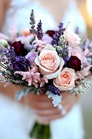 Romantic wedding bouquet with blush pink roses, deep burgundy flowers, and purple lavender sprigs creates elegant contrast against soft bokeh background.