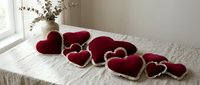 Red velvet heart-shaped pillows arranged on white bedding create romantic bedroom decor for Valentine's Day celebration and love-themed interior design.