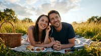 Happy couple enjoying romantic picnic on blanket in golden hour field with wicker basket and natural outdoor setting for leisure lifestyle content.
