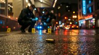Crime scene investigation with evidence markers on wet urban street at night with police officers and city lights creating atmospheric backdrop.
