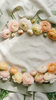 Delicate ranunculus flowers in soft pink and cream tones arranged with sage green ribbon on marble surface for wedding invitations and romantic designs.
