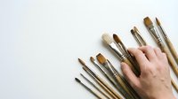 Artist hand holding paintbrushes of various sizes on white background, creative tools for painting, drawing, and art studio projects.