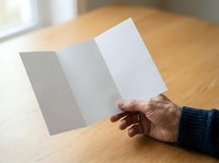 Mature adult hand holding open tri-fold brochure mockup on wooden table with natural light, suitable for marketing materials and promotional designs.
