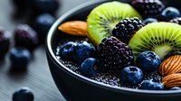Fresh berries, kiwi slices, and almonds in black bowl, healthy breakfast ingredients with antioxidants and superfoods on dark background, macro food photography.