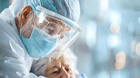 Healthcare worker in protective equipment examining elderly patient during pandemic, wearing surgical mask, face shield and medical gown in hospital setting.