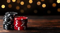 Stacks of black and red poker chips on dark wooden table with blurred golden bokeh lights in background creating atmospheric casino ambiance.