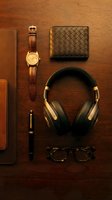 Luxury men's accessories flatlay on dark wood: leather wallet, gold watch, headphones, pen, glasses, and notebook for lifestyle blogs.