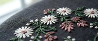 Delicate floral embroidery with pink and white daisies on dark fabric. Hand-stitched botanical design for fashion, crafts, and textile projects.