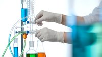 Laboratory technician in white gloves conducting chemical analysis with test tubes and scientific equipment in modern research facility.
