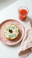 Bagel with cream cheese and chive letters spelling Good Day on a pink plate, served with fresh juice, bright morning breakfast concept.