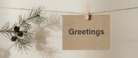 Kraft paper card with Greetings text hanging on rope with wooden clothespin, pine branch and cones, neutral beige background, holiday concept.