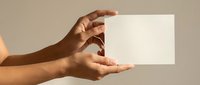 Hands holding blank white card with copy space for text or design on neutral beige background for business presentation or marketing materials.