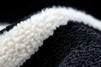 Extreme close-up macro photography of black and white wool textile showing detailed fiber texture and contrast between dark and light yarns in soft focus.