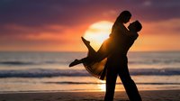 Romantic couple silhouette dancing on beach at sunset with dramatic orange purple sky and ocean waves creating intimate moment for love celebration.