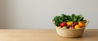 Fresh organic vegetables and fruits in wicker basket on wooden table against neutral background for healthy eating and nutrition concepts.