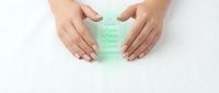 Female hands protecting green glass bottle with skincare serum or essential oil on white background. Natural beauty product protection concept.