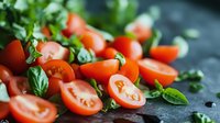 Fresh cherry tomatoes cut in halves with green basil leaves scattered on dark stone background, macro food photography with selective focus and bokeh effect.