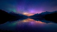 Tranquil mountain lake reflects vibrant aurora borealis and starry night sky, creating mirror-like symmetry with snow-capped peaks and colorful celestial display.