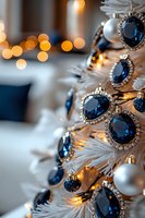 Elegant white Christmas tree decorated with sapphire blue jeweled ornaments and silver baubles, illuminated by warm bokeh lights creating festive luxury atmosphere.