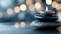 Burning candle on stacked zen stones against blurred golden bokeh background, creating peaceful spa atmosphere with soft focus and copy space.