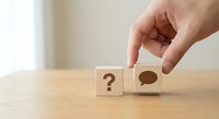 Hand placing wooden cube with speech bubble next to question mark block on table representing communication, decision making and problem solving concepts.