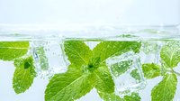 Fresh mint leaves and ice cubes floating in clear sparkling water with bubbles. Natural herbal drink ingredient for refreshing beverages and cocktails.