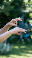Two hands reaching toward each other in protective gesture against blurred green nature background, symbolizing care, support and human connection outdoors.