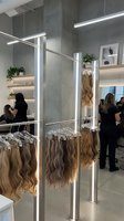 Modern hair extension salon interior with blonde wigs displayed on metal racks. Professional beauty business with LED lighting and concrete walls.