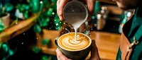 Barista pouring steamed milk into a latte art coffee cup, creating a beautiful rosette pattern in a cozy cafe setting.