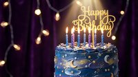 Blue galaxy birthday cake with lit candles and gold Happy Birthday topper, glowing bokeh lights on purple background, festive celebration.