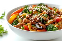 Stir-fried udon noodles with chicken, colorful vegetables, broccoli, bell peppers, and mushrooms topped with sesame seeds in white ceramic bowl.