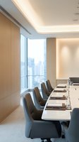Modern conference room with long white table, gray upholstered chairs, and floor-to-ceiling windows overlooking city skyline. Minimalist interior design with warm lighting and wood paneling for corporate meetings.