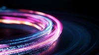 Glowing neon light trails in pink and blue colors create dynamic circular motion against dark background, abstract long exposure photography effect.
